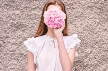 uma mulher segurando uma flor no rosto como quem não quer aparecer